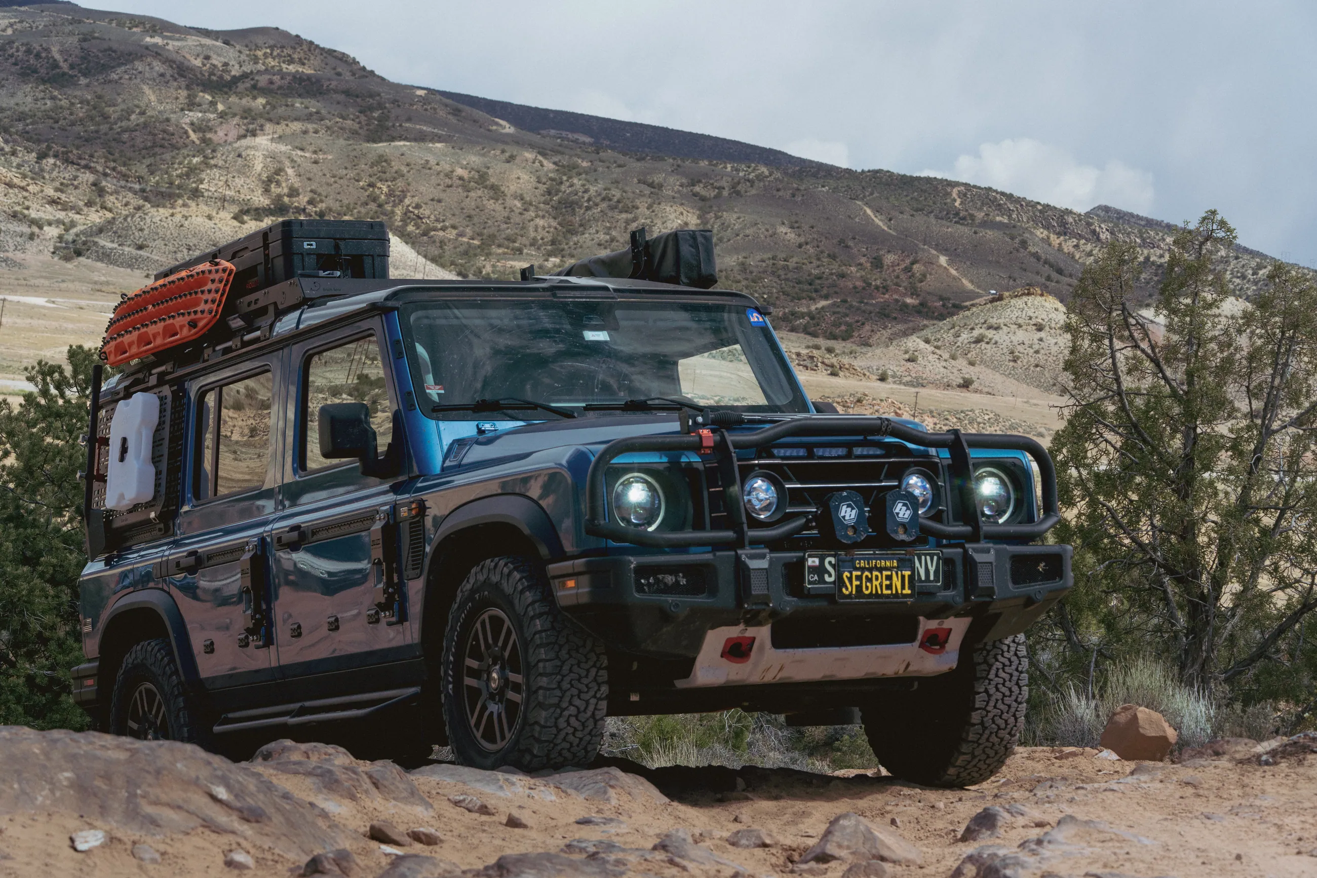 A blue Grenadier with a red roof rack on a desert trail