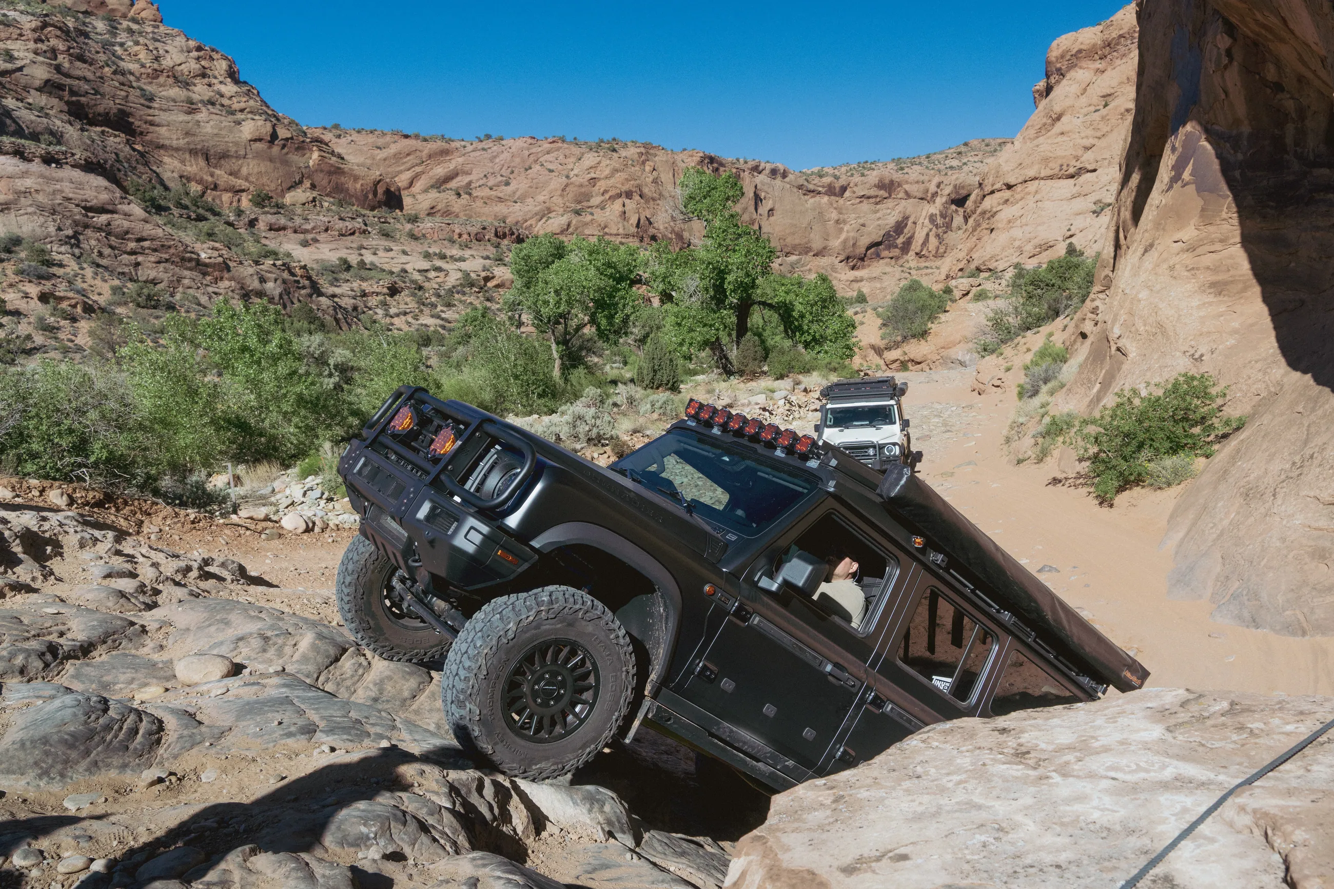 A black Grenadier tilted hard over a rock step in a sandy canyon