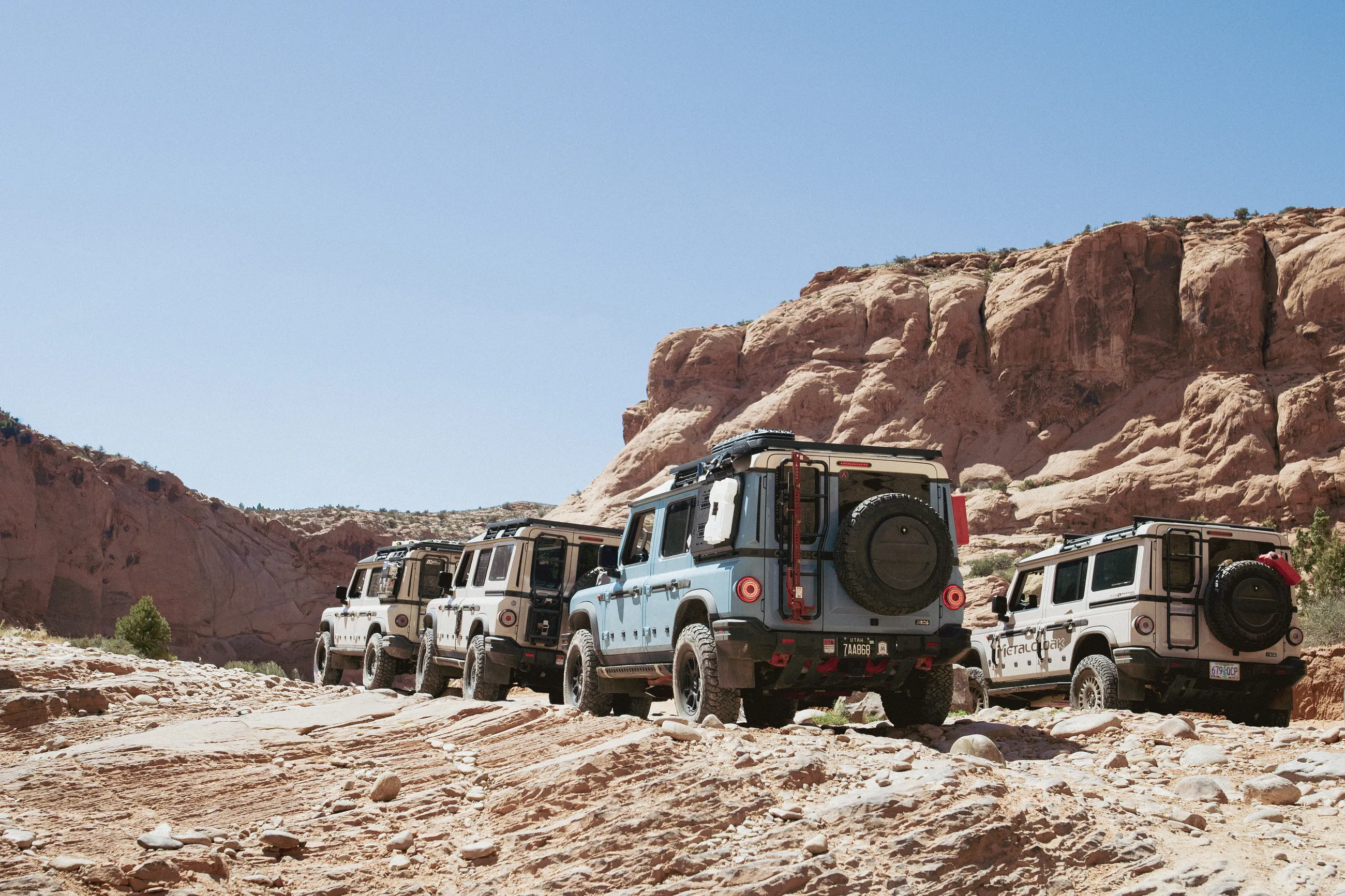 A convoy of INEOS Grenadiers on a rocky trail beneath red cliffs in Moab