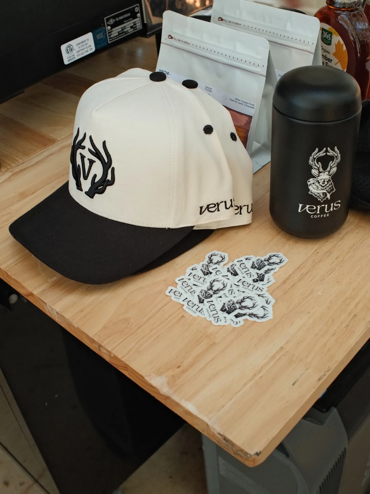 Cream-and-black Verus cap beside a black tumbler and deer-logo stickers
